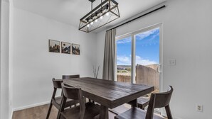 A dining area with a wooden table and chairs, a hanging light fixture, and a view through a sliding glass door. - Great for a group! Close and convenient! Fiber high speed internet! (Rock Springs)
