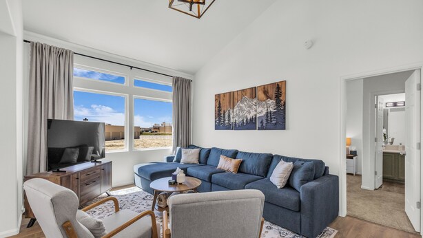 A modern living room with a sectional sofa, a TV, a dining area with a table and chairs, and a large window with a view. - Great for a group! Close and convenient! Fiber high speed internet! (Rock Springs)