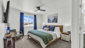 A bedroom with a bed, a ceiling fan, a window with curtains, a bedside table with a lamp, and a painting on the wall. - Great for a group! Close and convenient! Fiber high speed internet! (Rock Springs)