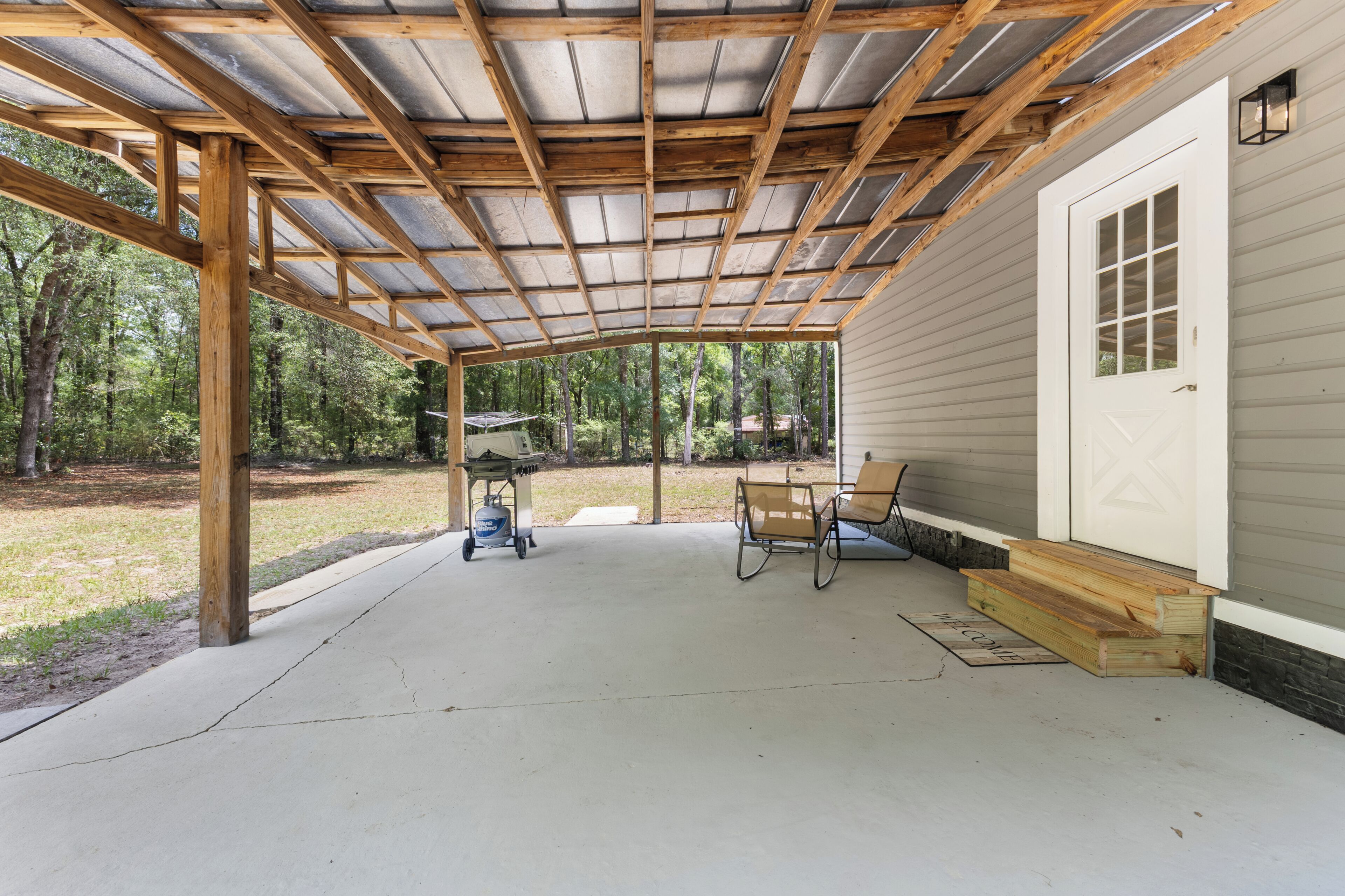 A covered patio with a concrete floor, wooden beams, a metal roof, and a bench.