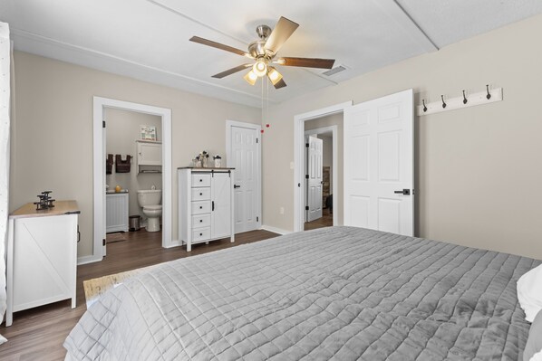 A bedroom with a bed, a ceiling fan, a white door, a coat rack, and a small desk.