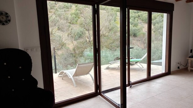 A room with a large sliding glass door leading to an outdoor patio with a table and chairs. - Andalusian Villa - Family Gatherings, Group Retreats & Nature Escapes (Iznajar)