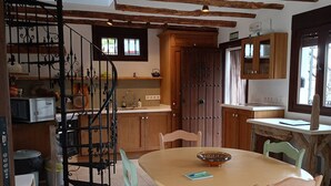 A rustic kitchen with wooden cabinets, a dining table with chairs, and a spiral staircase. - Andalusian Villa - Family Gatherings, Group Retreats & Nature Escapes (Iznajar)