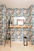 A room with a floral wallpaper, a wooden shelf, a black ladder, and a lantern.