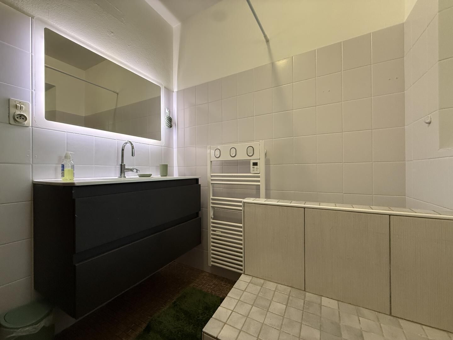 A modern bathroom with a large mirror, a black vanity, a shower area, and a towel rack.