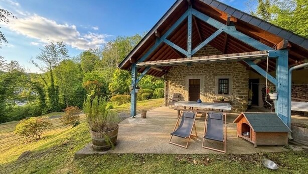 Edificio de piedra con techo de madera, un patio con dos sillones de descanso y una caseta para perro.