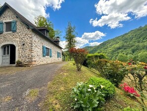 A stone house with a gravel driveway, surrounded by lush greenery and a mountainous backdrop. - ONDARIA - LICQ ATHEREY (LICQ ATHEREY)