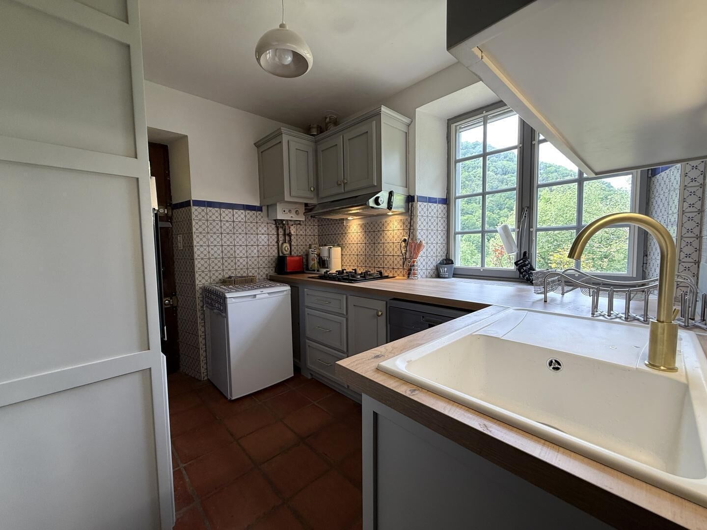 Une cuisine de taille réduite, équipée d’un évier, d’une cuisinière et d’une fenêtre laissant entrer la lumière naturelle.