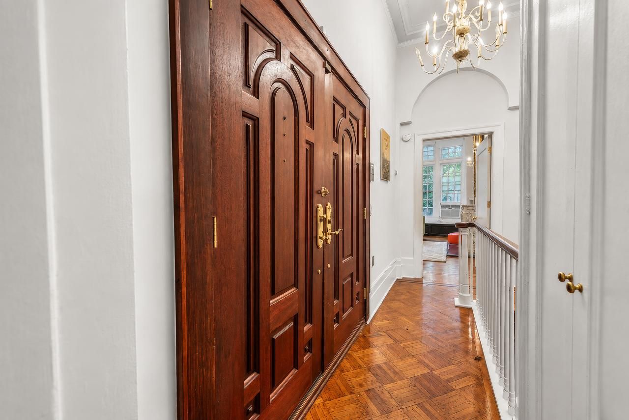 A hallway with a wooden door, white walls, and a chandelier.