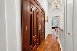 Un pasillo con puerta de madera, paredes blancas y un candelabro.