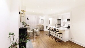 A modern kitchen with white cabinetry, a central island with bar stools, and a dining area with a round table and chairs. - Luxury 4-Bedroom UES Townhouse with Private Deck and Garden (New York)