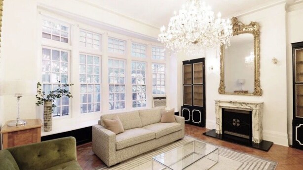 A room with a sofa, a glass coffee table, a chandelier, a fireplace, and large windows. - Luxury 4-Bedroom UES Townhouse with Private Deck and Garden (New York)