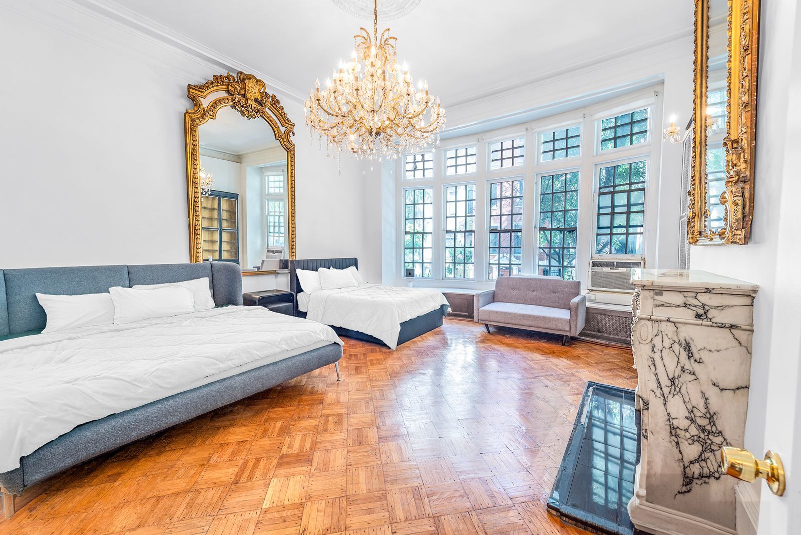 A spacious bedroom with a large bed, a sofa, a chaise lounge, and a marble fireplace.