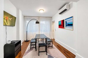Una sala moderna con una mesa larga de comedor, una lámpara de pie negra y un televisor de pantalla plana montado en la pared.