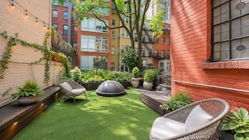 A courtyard with artificial grass, two wicker chairs, potted plants, and a dome-shaped seating area.