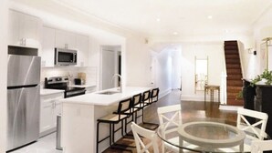 A modern kitchen with stainless steel appliances, a central island with chairs, and a staircase leading to another level. - Luxury 4-Bedroom UES Townhouse with Private Deck and Garden (New York)