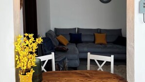 En matplats med ett träbord, två hängande taklampor, en vas med gula blommor och en grå soffa i bakgrunden.