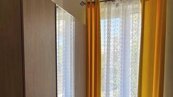 A room with a wardrobe, a window with yellow curtains, and a view of trees.