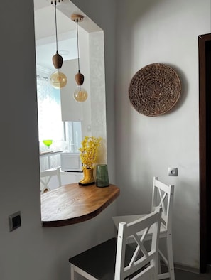 A dining area with a wooden table, a white chair, a mirror, and a woven wall decoration.