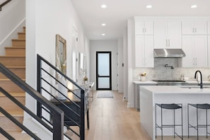 A modern kitchen with white cabinets, a stainless steel range hood, and a central island with bar stools. - Pool + Sauna | 2 Homes for Groups | Sleeps 14 | (Austin)