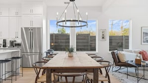 Et moderne køkken med hvide skabe, et rustfrit stål køleskab, et træspisebord med stole og en hængende lampe.