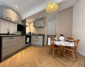 A modern kitchen with wooden cabinets, a dining area with a table and chairs, and a pendant light. - PEONTENIA - BIDARRAY (BIDARRAY)