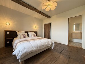 A bedroom with a large bed, wooden beams, a ceiling fan, and a bathroom with a mirror and sink. - PURTAUNIA - BEGUIOS - Gîte (BEGUIOS)