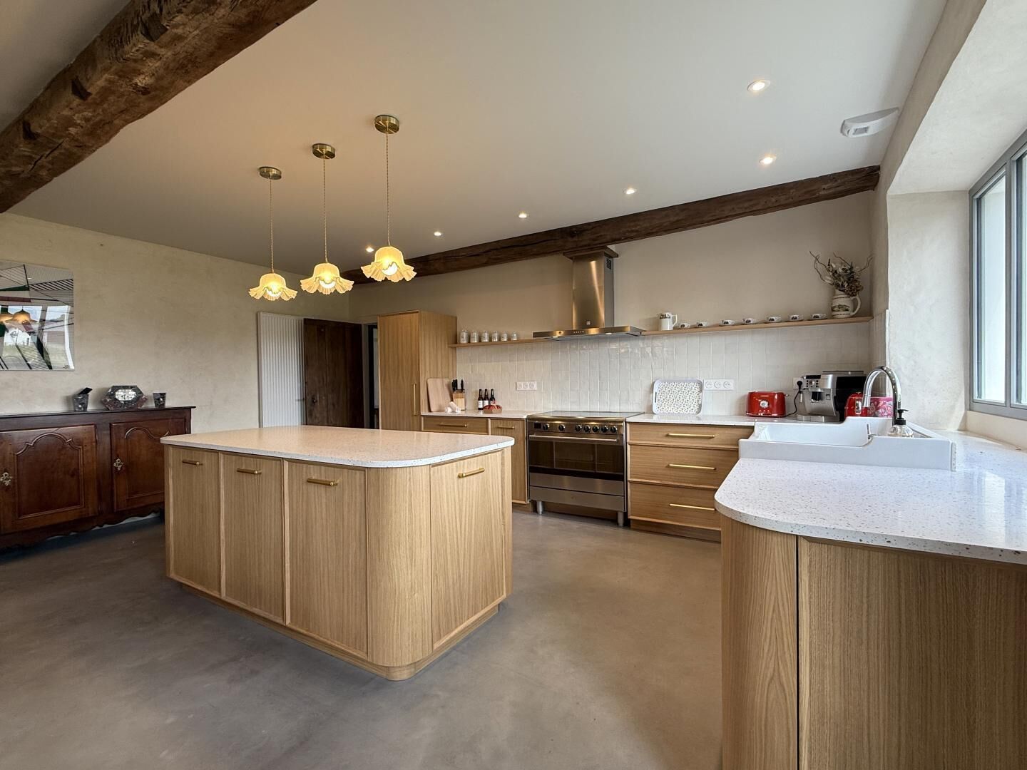 A modern kitchen with a central island, wooden cabinets, stainless steel appliances, and pendant lighting.