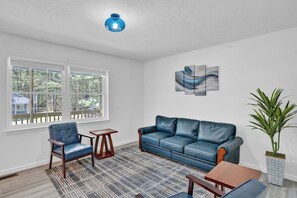 Un soggiorno con un divano in pelle blu, un tavolino in legno, una poltrona blu, un tappeto decorato e una pianta in vaso.