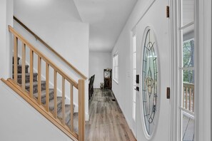 Un pasillo con escalera de madera, puerta de cristal con diseño decorativo y vista al exterior.
