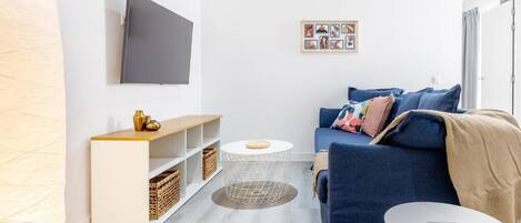 Una sala de estar moderna con un sofá, un televisor, una mesita redonda y una estantería.