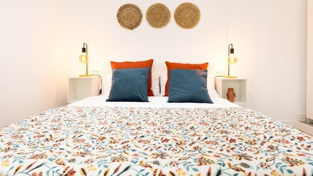 A bed with a floral-patterned bedspread, two pillows, and two bedside lamps. - Carine Laguna (San Cristobal de La Laguna)
