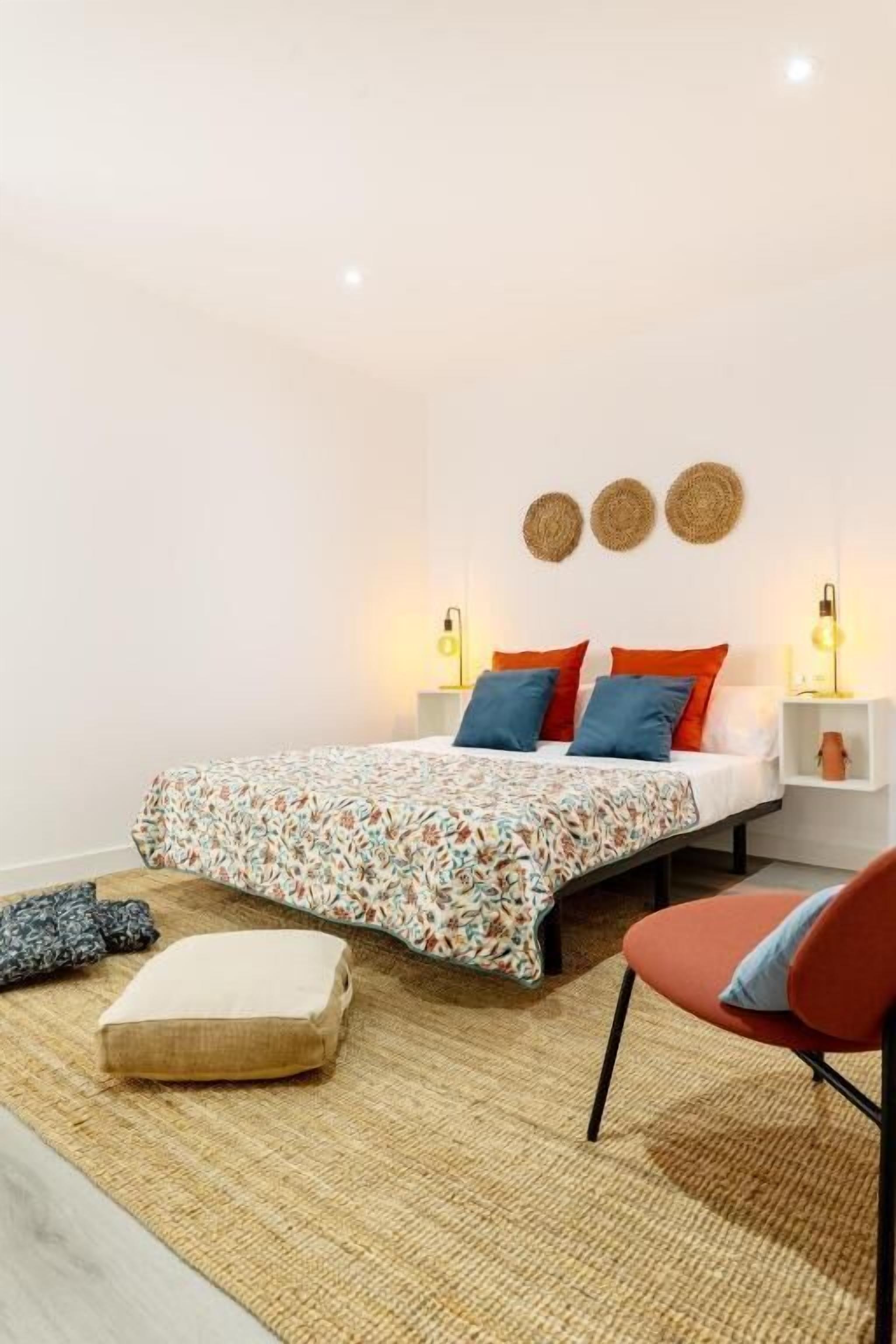 A bedroom with a bed, pillows, a chair, a bedside table, and wall decor.
