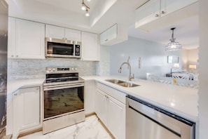Een moderne keuken met roestvrijstalen apparatuur, witte kasten en een marmeren achterwand.