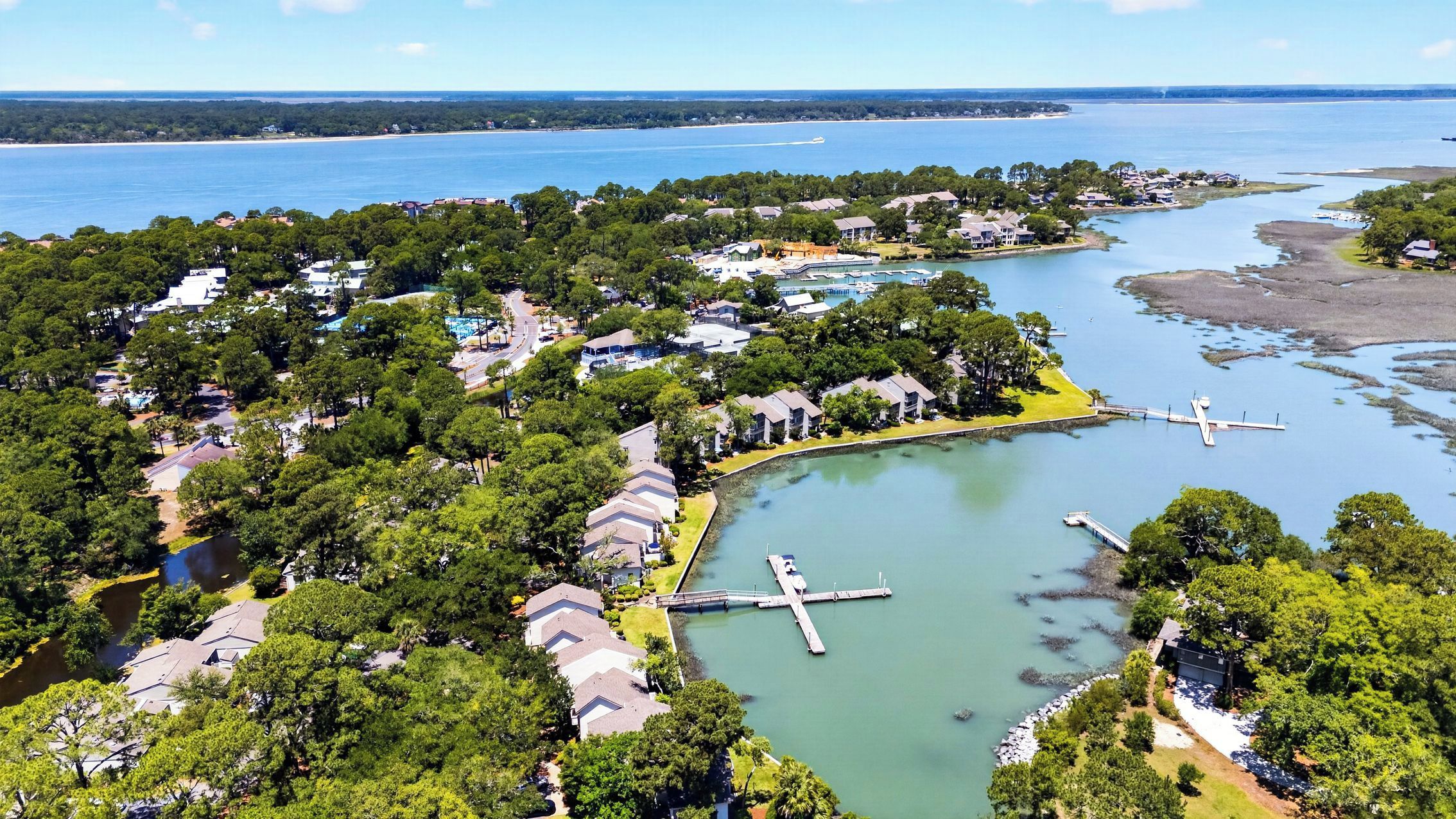 An aerial view of a coastal residential area with houses, a marina, and a large body of water.