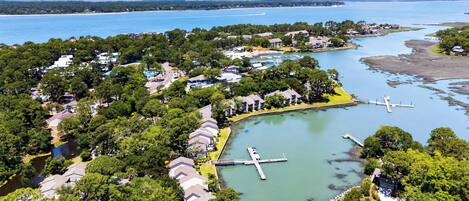 An aerial view of a coastal residential area with houses, a marina, and a large body of water.