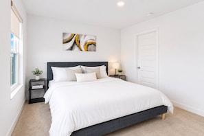 A bedroom with a bed, a nightstand, a lamp, a door, and a window.
