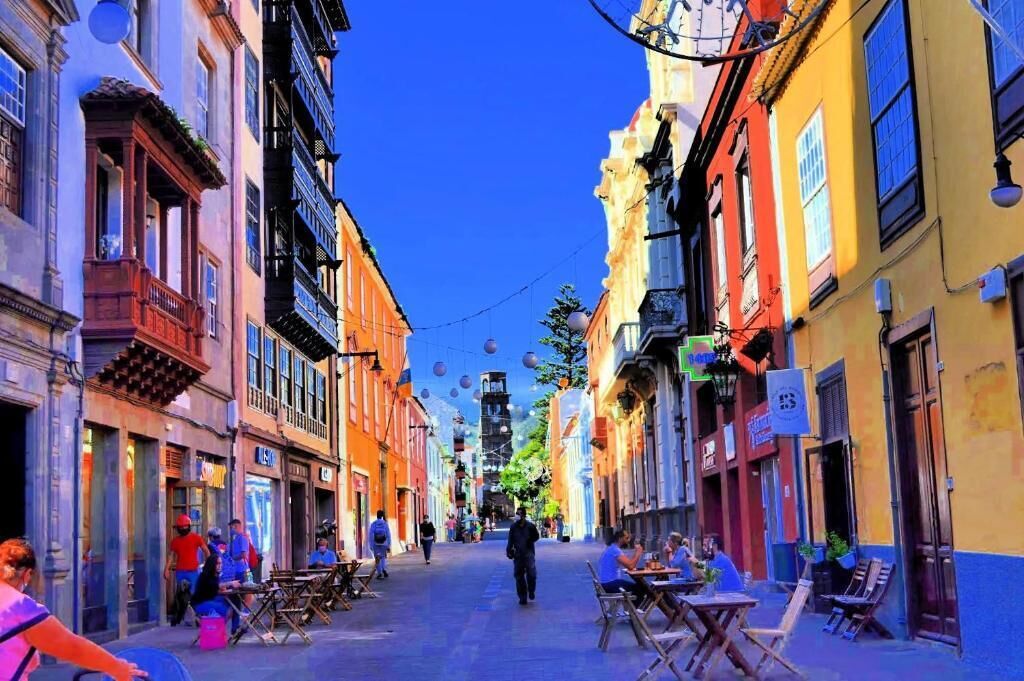 Une rue bordée d’immeubles, agrémentée de terrasses et décorée de guirlandes.