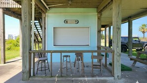 A covered outdoor bar area with a closed shutter, wooden stools, and a bench. - Fully fenced, pet friendly, 3-bedroom, 2 full bath on the beach side, sleeps 10 (Bolivar Peninsula)