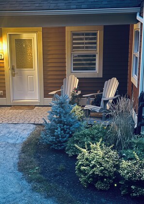 A house with a front door, two Adirondack chairs, a small Christmas tree, and a brick pathway. - Le Refuge Douillet in the heart of Tremblant: ski, bike, pool and spa (Mont-Tremblant)