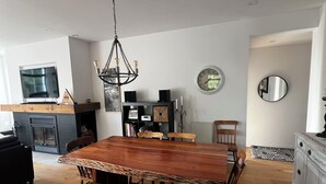 A dining area with a wooden table and benches, a chandelier, a television, and a fireplace. - Le Refuge Douillet in the heart of Tremblant: ski, bike, pool and spa (Mont-Tremblant)