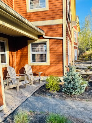 A wooden house with a porch, two Adirondack chairs, and a small garden. - Le Refuge Douillet in the heart of Tremblant: ski, bike, pool and spa (Mont-Tremblant)