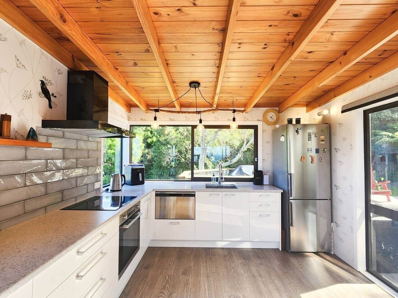 Una cucina moderna con travi in legno, lavastoviglie integrata, elettrodomestici in acciaio inossidabile e un'ampia finestra.