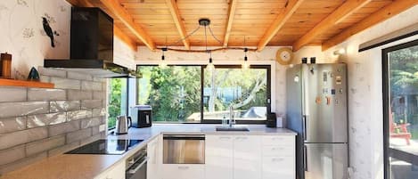 A modern kitchen with wooden beams, a built-in dishwasher, stainless steel appliances, and a large window.