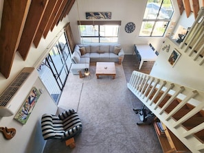 A loft-style living space with a high ceiling, a large window, a sofa, a coffee table, and a staircase.