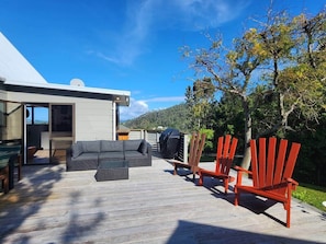 A deck with outdoor furniture, a grill, and a view of a mountainous landscape.