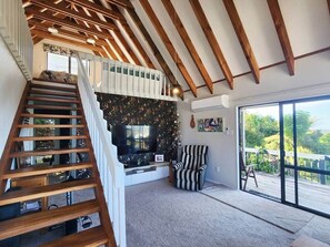 A staircase leading to a balcony, a flat-screen TV, a striped armchair, and a large sliding glass door.