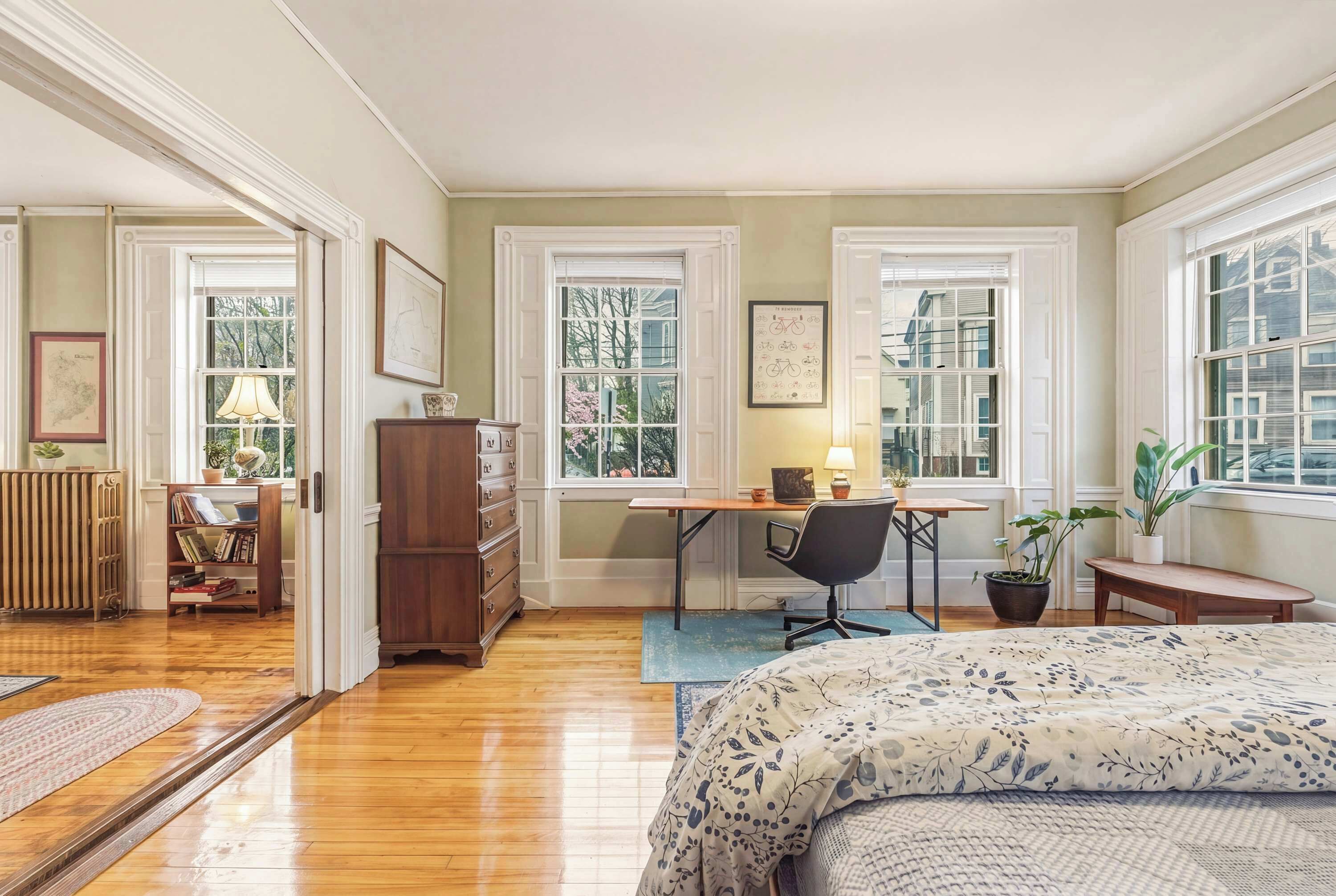A bedroom with a bed, desk, chair, and large windows.