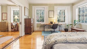Une chambre à coucher avec un lit, un bureau, une chaise et de grandes fenêtres.