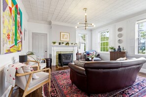 Ein Wohnzimmer mit Kamin, einer Ledersofa, einem gemusterten Teppich und einem großen abstrakten Gemälde an der Wand.